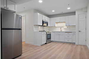 Kitchen with light countertops, white cabinetry, stainless steel appliances, and light wood-style floors