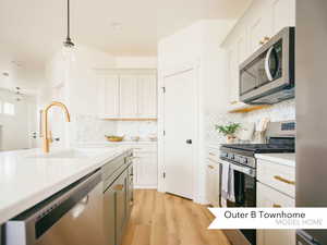 Kitchen featuring decorative backsplash, a sink, light countertops, light wood finished floors, and stainless steel appliances
