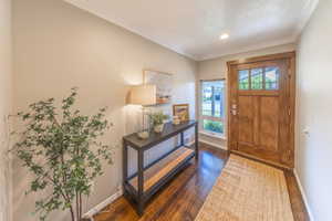 Foyer entrance featuring baseboards, a textured ceiling, dark wood-style flooring, and crown molding
