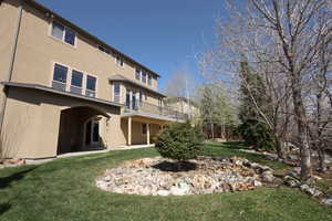 Rear view of house featuring a lawn, stucco siding, a balcony, and a patio