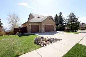 View of home's exterior with fence, stone siding, a garage, concrete driveway, and a yard