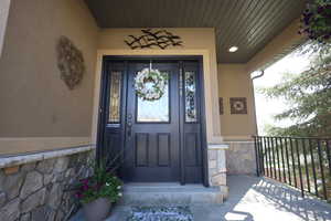 View of exterior entry featuring a porch, stone siding, and stucco siding
