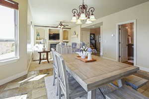 Dining space featuring baseboards, a tiled fireplace, ceiling fan with notable chandelier, and stone tile flooring