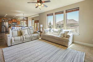 Living room with recessed lighting, baseboards, ceiling fan with notable chandelier, and dark colored carpet