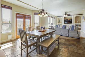 Dining space with baseboards, ceiling fan with notable chandelier, stone tile flooring, and visible vents