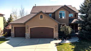 View of front of home with a garage, stone siding, stucco siding, a shingled roof, and concrete driveway