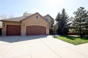 View of front facade featuring a garage, a front yard, stone siding, stucco siding, and driveway