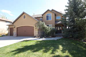 View of front of house with driveway, a garage, a front lawn, stone siding, and stucco siding