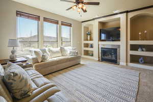 Living room with carpet floors, built in features, a tiled fireplace, a ceiling fan, and baseboards