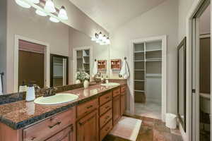 Full bath with double vanity, a sink, vaulted ceiling, and a spacious closet