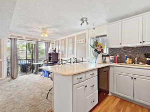 Kitchen featuring a sink, light countertops, a peninsula, a ceiling fan, and white cabinetry
