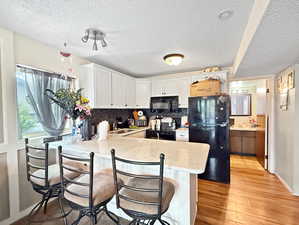 Kitchen with a sink, black appliances, a peninsula, and a textured ceiling