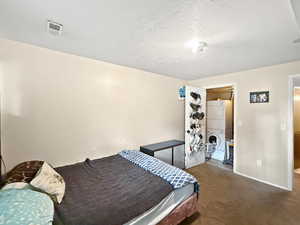 Bedroom with baseboards, a textured ceiling, carpet, and stacked washer / drying machine