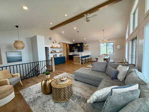 Living area featuring  beam ceiling, high vaulted ceiling, ceiling fan with notable chandelier, and light wood-style flooring