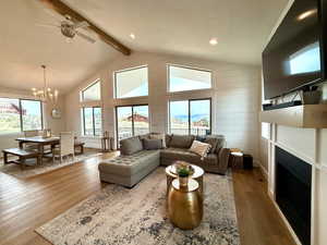 Living area with a fireplace, high vaulted ceiling, ceiling fan with notable chandelier, wood finished floors, and beamed ceiling