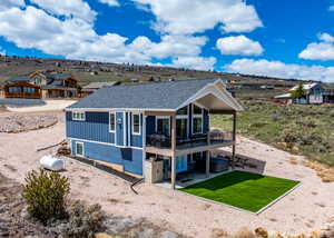 Rear view of house featuring a shingled roof, board and batten siding, a deck, a patio area, and a lawn