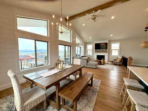Dining space featuring a fireplace, beamed ceiling, high vaulted ceiling, light wood-type flooring, and ceiling fan with notable chandelier