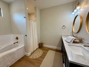 Bathroom with double vanity, wood finished floors, baseboards, a bath, and a sink