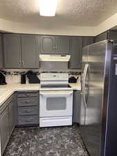 Kitchen with under cabinet range hood, stainless steel fridge with ice dispenser, backsplash, gray cabinets, and electric range