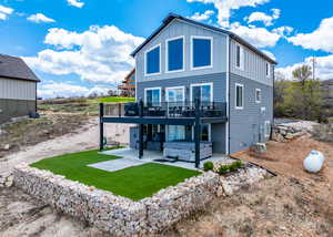 Rear view of property with a deck, board and batten siding, a patio area, a lawn, and a hot tub