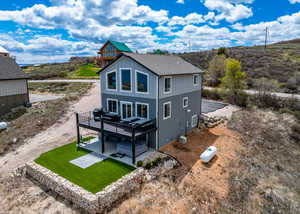 Rear view of house featuring a deck, roof with shingles, a patio area, board and batten siding, and a yard