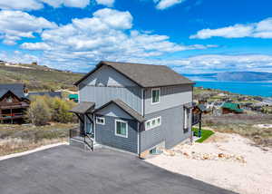 View of property exterior with a water view, driveway, and a shingled roof