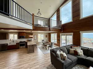 Living room with plenty of natural light, a towering ceiling, light wood-type flooring, wooden walls, and an inviting chandelier