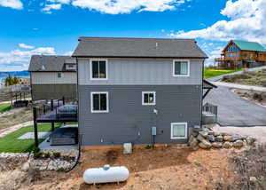 Back of property featuring board and batten siding, a patio, a shingled roof, and a wooden deck