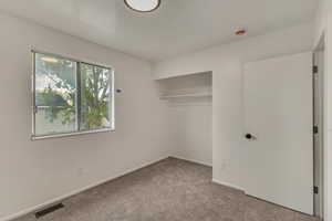 Unfurnished bedroom with carpet floors, baseboards, visible vents, and a closet