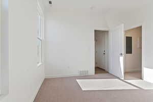 Unfurnished room with baseboards, electric panel, light colored carpet, and visible vents