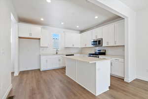 Kitchen with a center island, a sink, light wood finished floors, stainless steel appliances, and white cabinetry