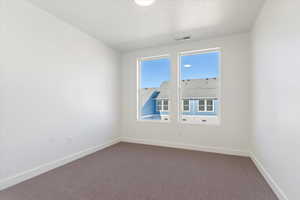 Unfurnished room featuring visible vents, baseboards, and dark colored carpet