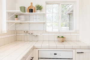 Room details with tasteful backsplash, open shelves, tile countertops, and wall oven