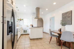 Kitchen featuring white oven, light tile patterned floors, tile counters, island exhaust hood, and stainless steel refrigerator with ice dispenser