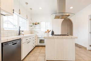 Kitchen with tile counters, light tile patterned floors, island exhaust hood, tasteful backsplash, and appliances with stainless steel finishes