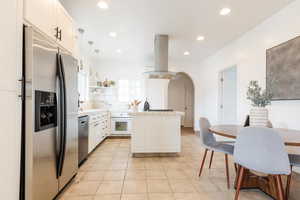 Kitchen with recessed lighting, tile countertops, arched walkways, island range hood, and appliances with stainless steel finishes