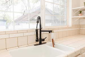 Interior details with cream cabinetry, tile counters, decorative backsplash, and a sink