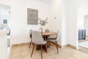 Dining room featuring light tile patterned flooring, arched walkways, ceiling fan, and baseboards