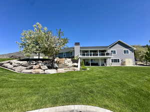 Grand back of house with a yard, a chimney, and a deck and patio