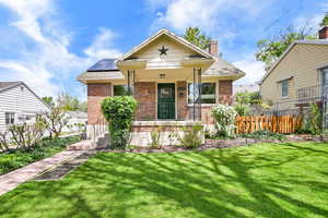 View of front facade featuring fence, brick siding, a front yard, a chimney, and solar panels