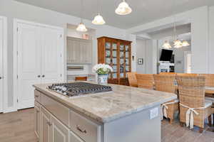 Kitchen featuring an inviting chandelier, stainless steel gas cooktop, a kitchen island, light stone counters, and tiled floors