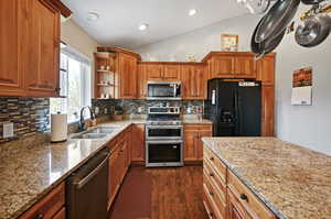 Kitchen featuring light stone countertops, a sink, stainless steel appliances, dark wood-type flooring, and vaulted ceiling