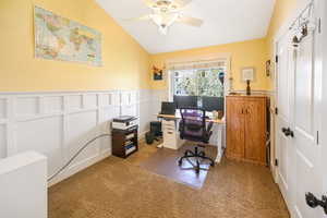 Home office featuring carpet floors, a decorative wall, lofted ceiling, a wainscoted wall, and a ceiling fan