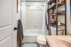 Full bathroom with vanity, shower / bathtub combination with curtain, and toilet