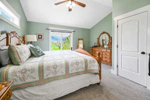 Carpeted bedroom with ceiling fan, vaulted ceiling, and access to exterior