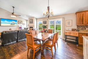 Dining room with ceiling fan with notable chandelier, recessed lighting, vaulted ceiling, dark wood-type flooring, and a lit fireplace