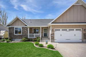 Craftsman-style home with board and batten siding, driveway, covered porch, and stone siding