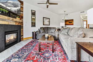 Living area featuring wood finished floors, ceiling fan with notable chandelier, a fireplace, baseboards, and visible vents