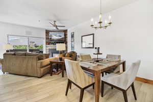 Dining area with baseboards, ceiling fan with notable chandelier, light wood finished floors, and a glass covered fireplace