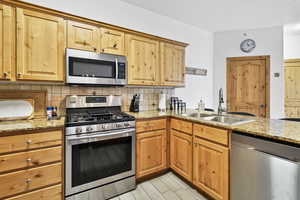 Kitchen featuring tasteful backsplash, light stone counters, appliances with stainless steel finishes, and a sink